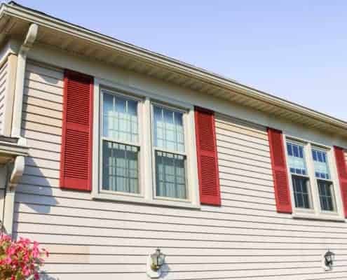Light Tan color right side of the house with two sets of double-hung vinyl energy efficient windows with decorative red shutters on both sides of the windows